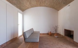 Interior view of the living area at Casa Modesta featuring white walls, tiled floors, arched brick ceiling, a grey sofa, a fireplace, terracotta pots and a door