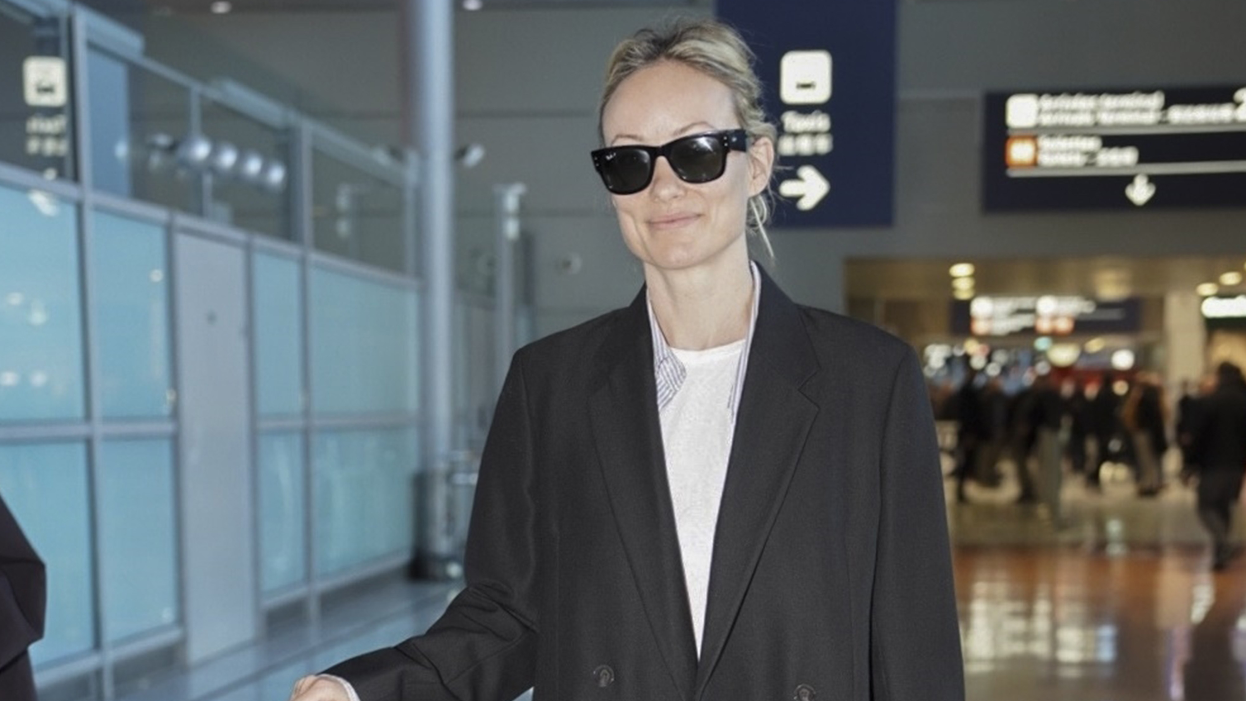 Olivia wears a black blazer with a white tee and black glasses.