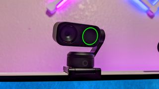 The Insta360 Link 2 webcam installed on a monitor and turned on, showing its green ring LED indicator.