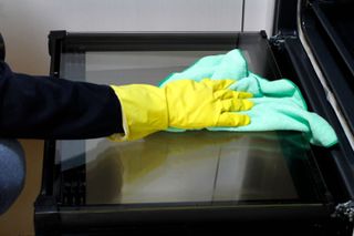 A close up of a person wiping the glass door of an oven with a cloth