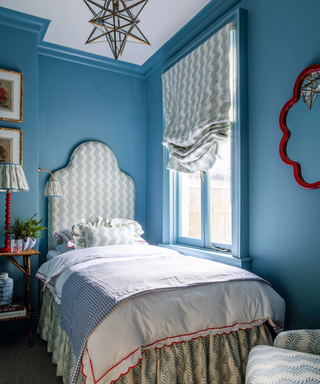 bedroom with blue walls and patterned ottoman and vallance and bobbin lamp in red with red scallop edged mirror