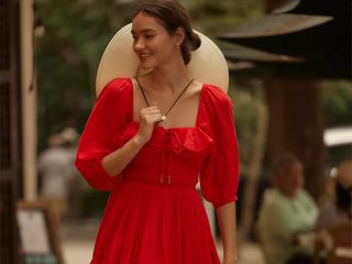 model wears red dress and sun hat while walking down a street