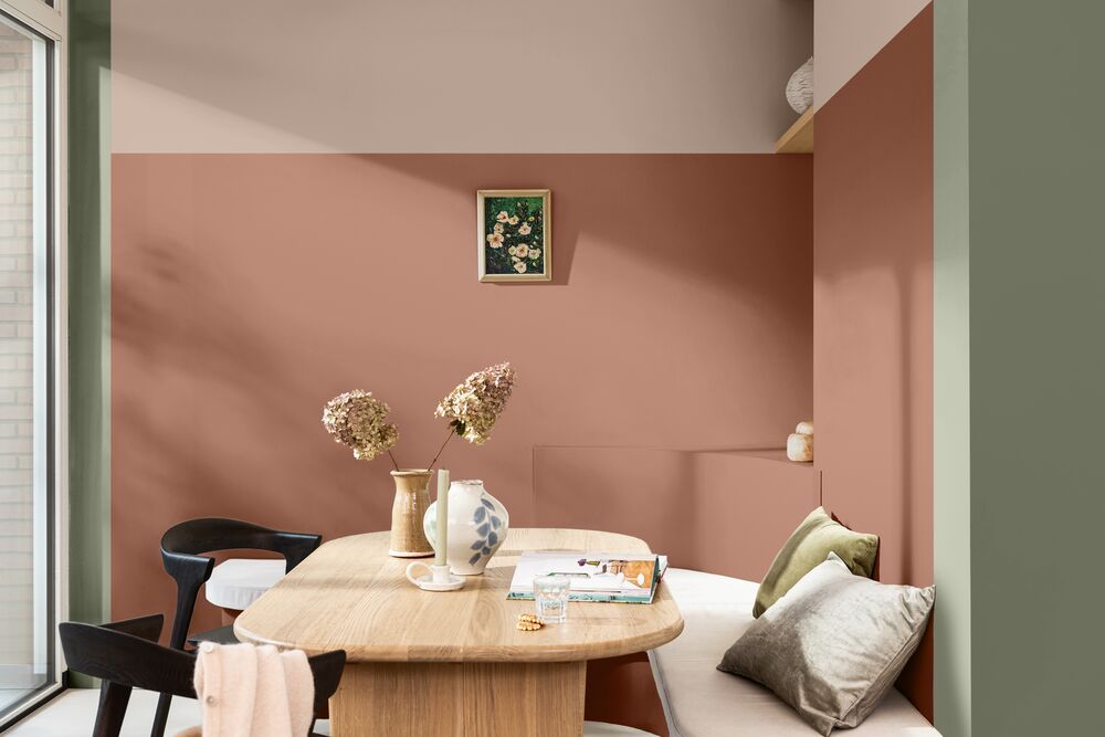A breakfast nook with terracotta and lighter pink color blocked walls and sage green trim. The table is a wooden oval and there is a white bench seat.