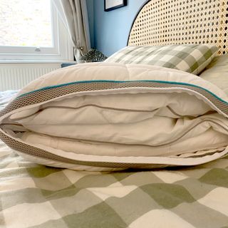 The Simba Hybrid Firm pillow unzipped to show the three inner layers on a bed with a green and white checked duvet