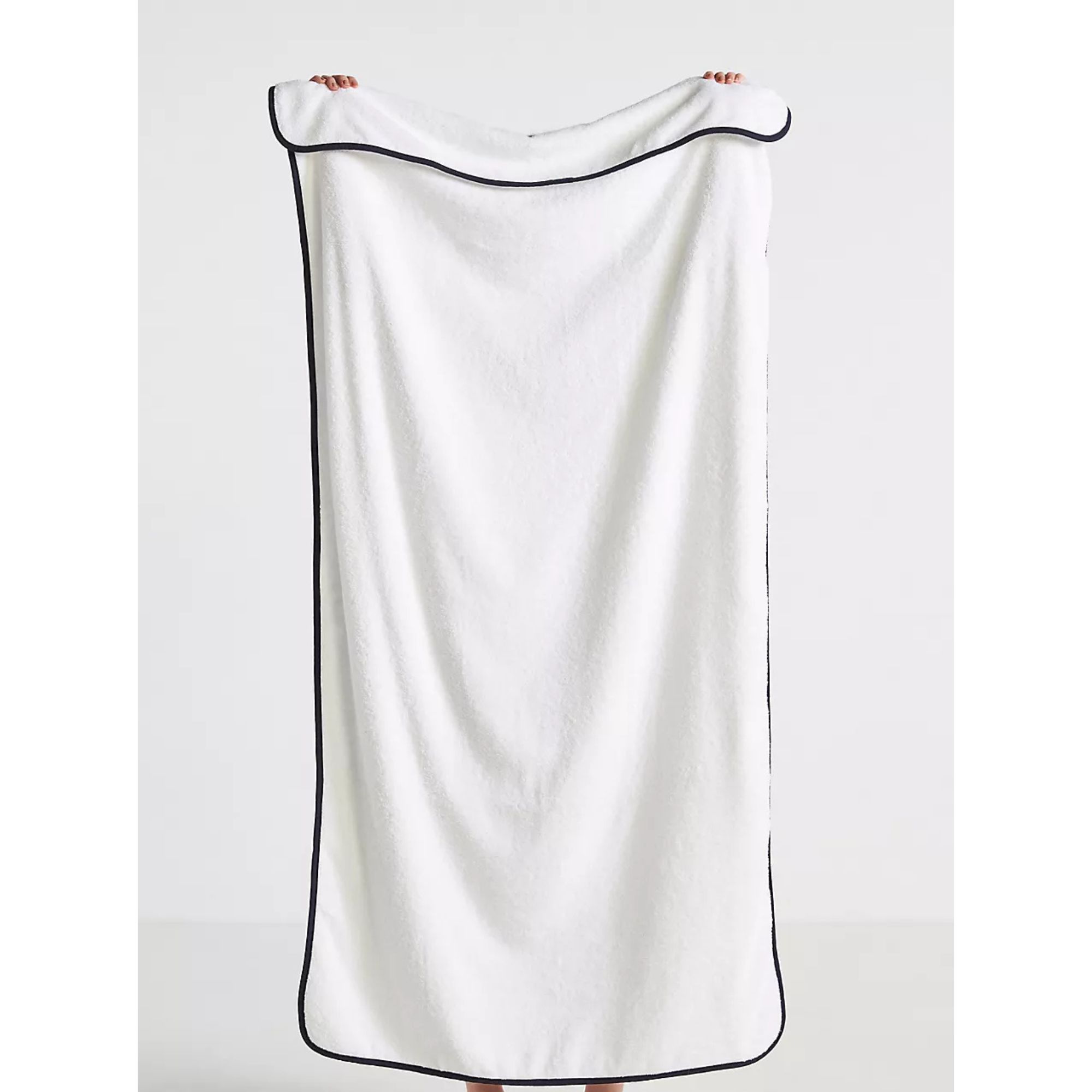 A white cotton towel with black piped edges being held up.