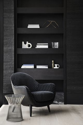 Black chair and black wooden wall shelves with books on behind