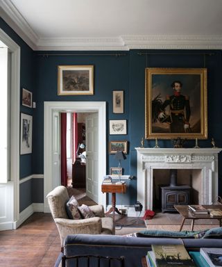 traditional living room with dark blue walls, white trim and ceiling, wooden flooring, gallery wall with traditional artwork and fireplace with wood burner