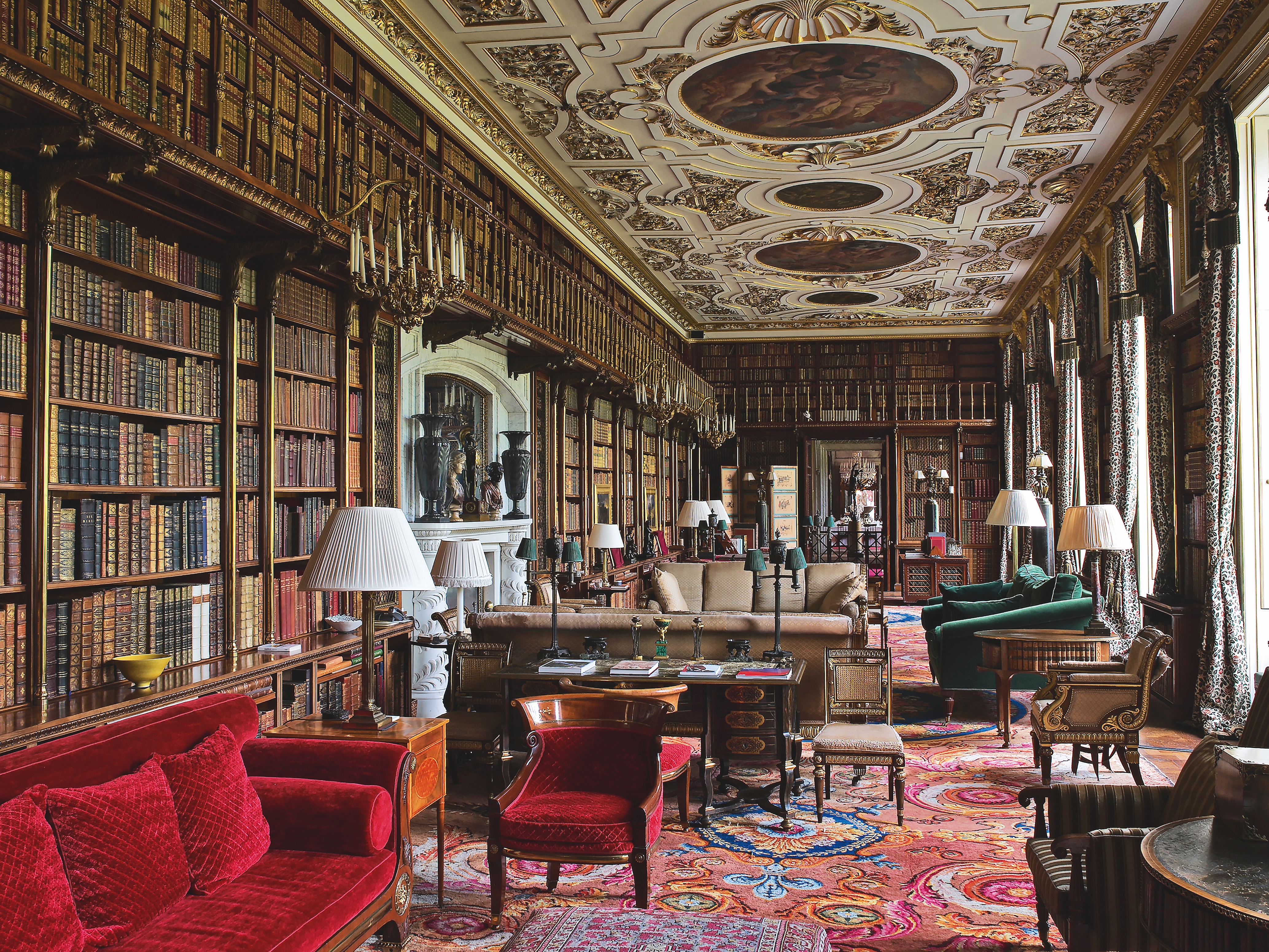 Grand library room with lots of antique furniture and an ornate gold and white ceiling