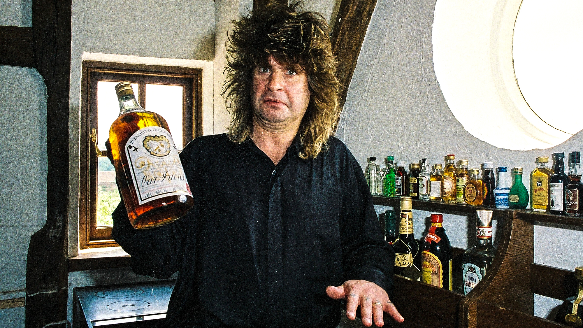 Black Sabbath singer Ozzy Osbourne holding a large bottle of whiskey at his home in 1988. 