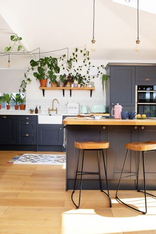 Dark blue Shaker kitchen with wood and black metal bar stools, bare bulb pendants, and oak-style flooring