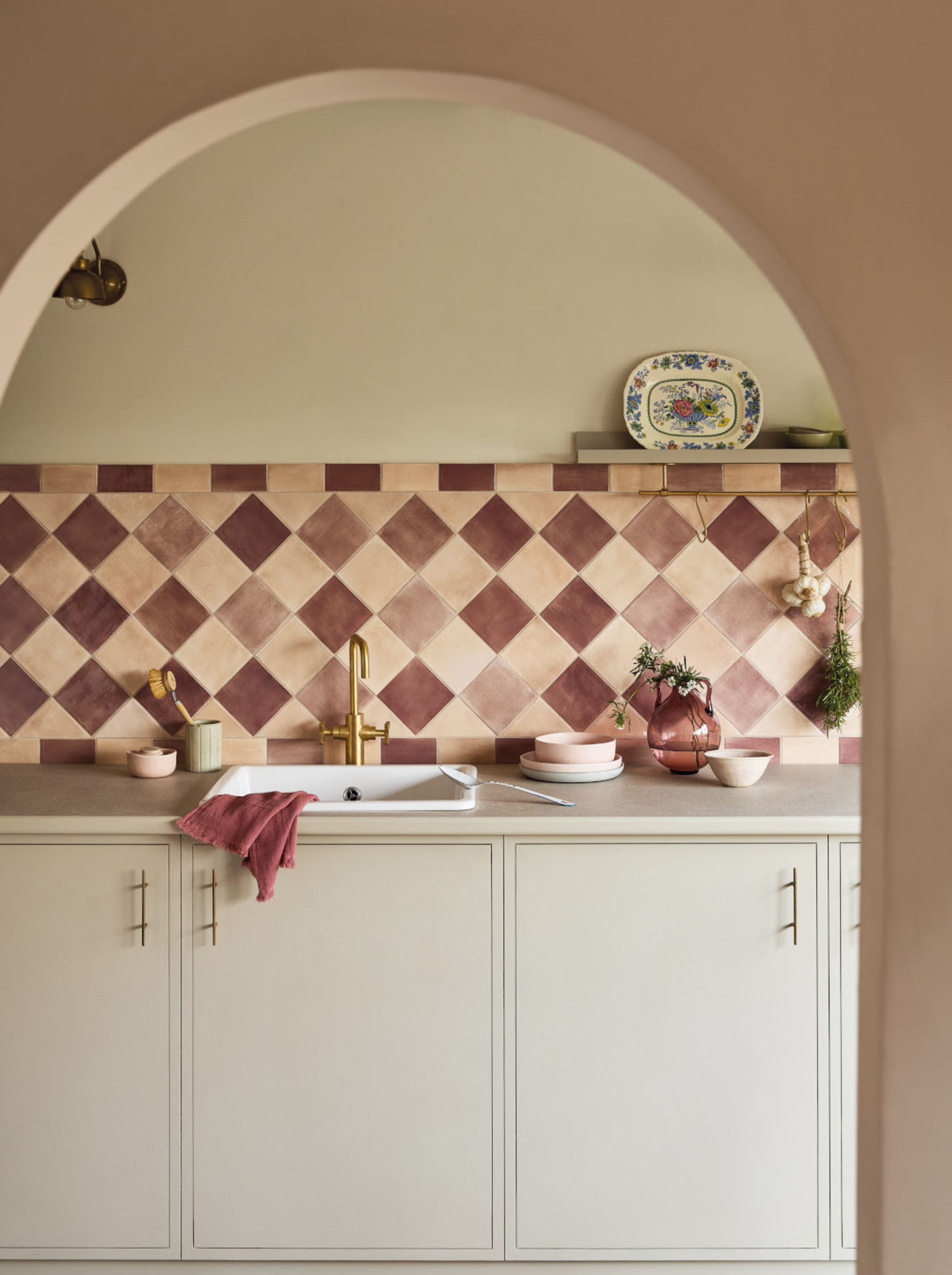 Image of a beige kitchen counter with a pink gingham backsplash. The doorway into the kitchen is curved.