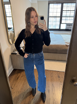 Nikki wears barrel-leg jeans, a black cardigan, and black ankle boots.