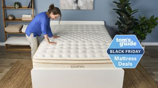 The image shows a dark haired woman wearing a blue shirt and beige trousers placing her hands on the top of a cream and gold mattress, placed on a white bed frame in a neutrally decorated bedroom. On the top of the image a badge reads 'Tom's Guide Black Friday Mattress Deals'