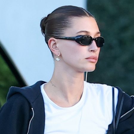 Hailey bieber wears black sunglasses, a white tee, and a black zip-up hoodie.