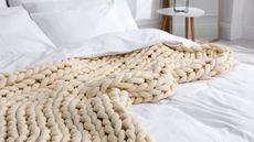 Cream colored chunky knit blanket on white bed