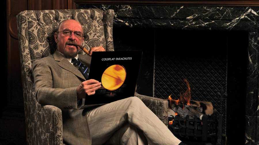 Ian Anderson sitting in a leather chair holding a copy of Coldplay&#039;s Parachutes