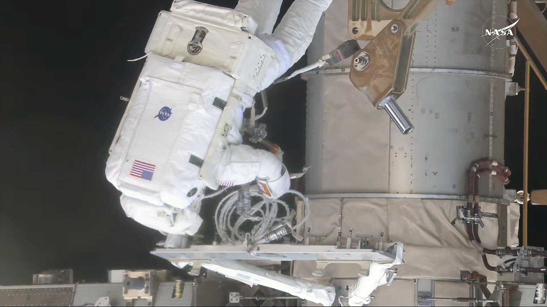 an astronaut in a white spacesuit works outside a space station