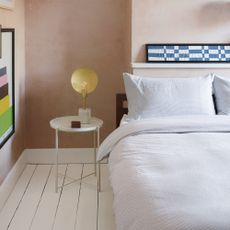 A bedroom with plaster pink walls, striped bedlinen on a double bed, and a statement bedside lamp