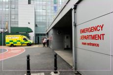 A close up of a sign reading 'emergency department' with an ambulance in the background