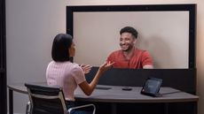 A woman sat at a desk in front of the HP Dimension 3D video communication technology screen, using Google Beam technology, talking to a man on the screen.