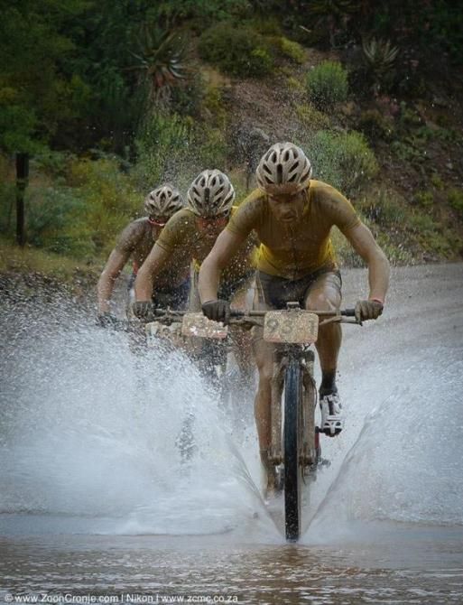 RE:CM's Waylon Woolcock leads teammate Erik Kleinhans and EAI Cycling's Johann Rabie through a puddle during Stage 6