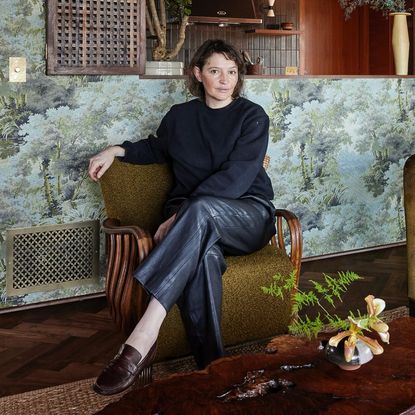 shoe designer jamie haller sits on an armchair in front of a wallpaper wall