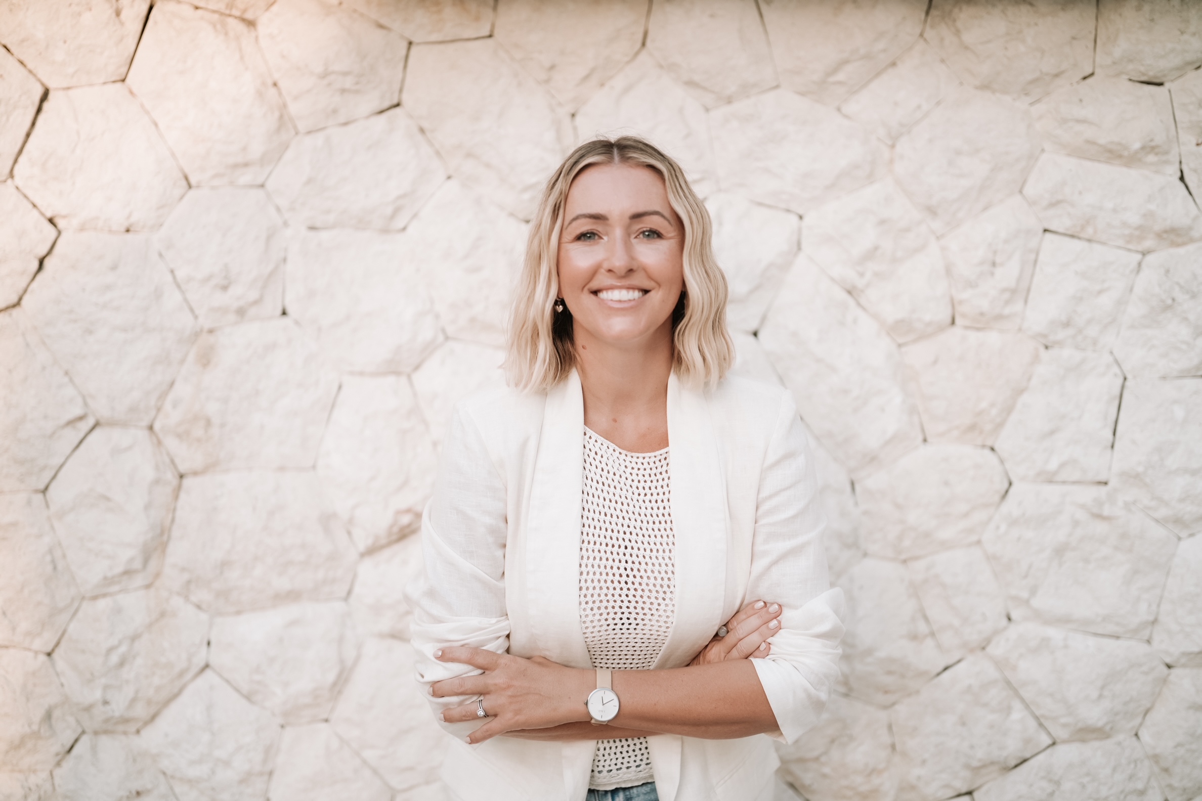 A woman standing with her arms crossed against a white terazzo brick wall