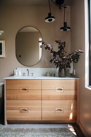 A bathroom wooden vanity unit with quirky pendant lamp and eucalyptus styled on the top surface