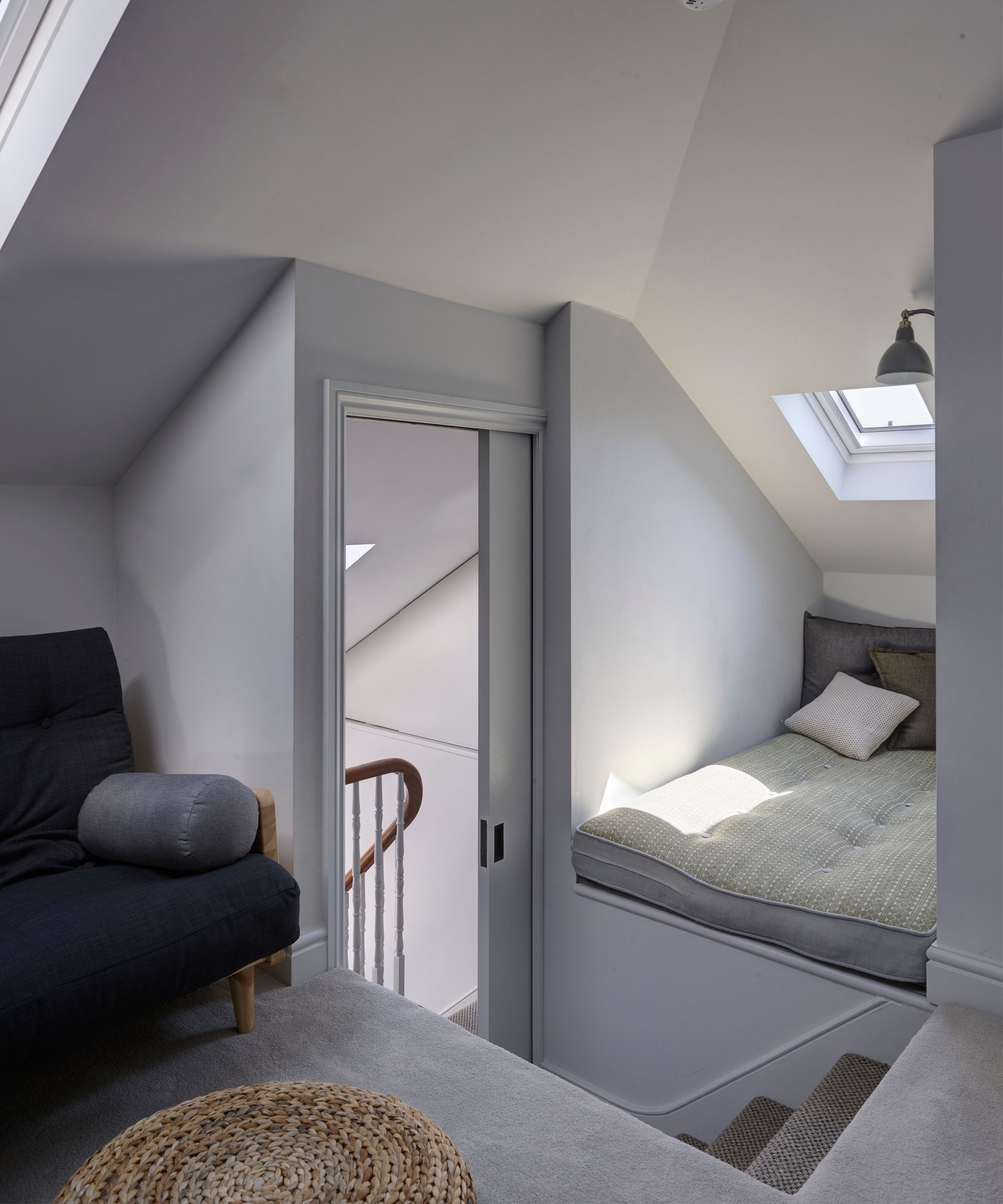 A bright attic space with a sliding door, futon mattress, blue upholstered chair and rattan stool