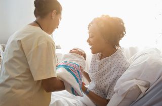 A nurse hands a mother her newborn baby
