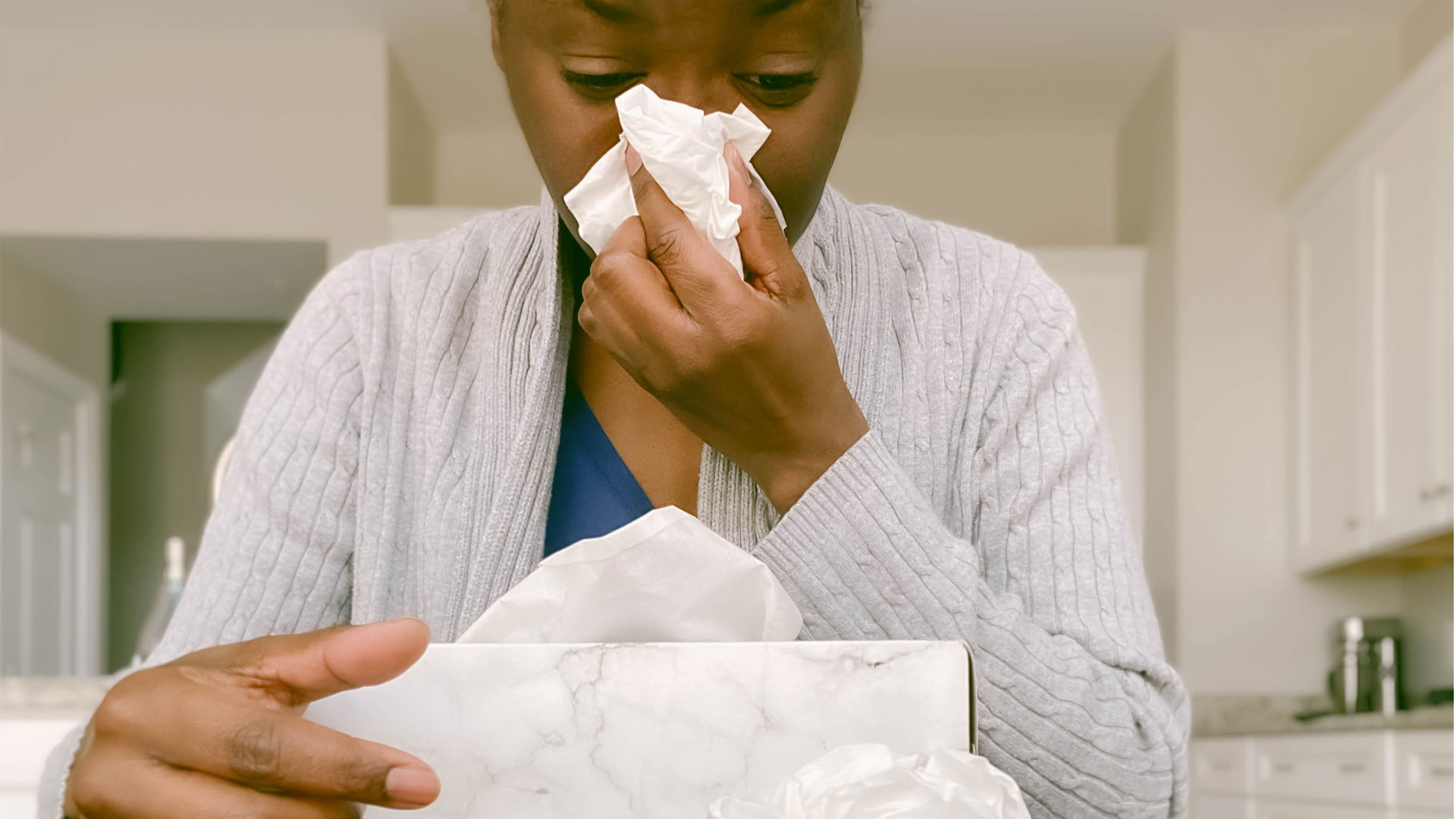 Image shows woman blowing her nose with a tissue