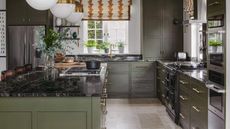 A dark green kitchen with large pendant lights and a kitchen island