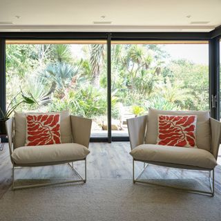 Two chairs with red patterned cushions in front of dark frame sliding patio doors