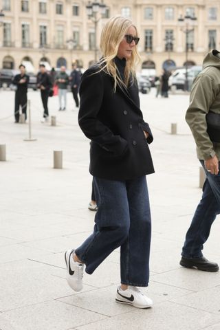 Gwyneth Paltrow wears Nike Cortez sneakers in white with wide leg jeans and a black pea coat.