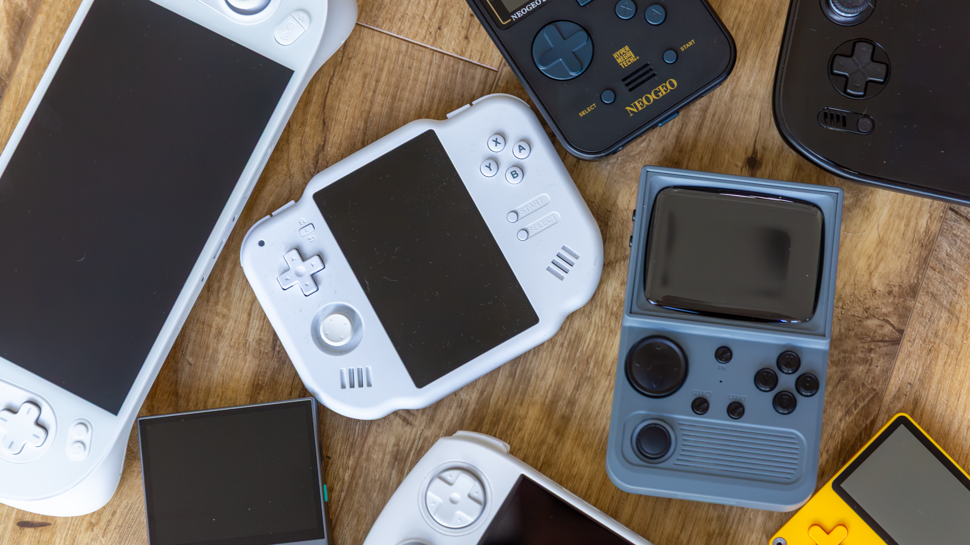 Multiple retro gaming handhelds on a wooden floor