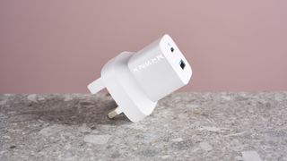 Anker 323 Charger (33W) balanced on its prongs against a pink background