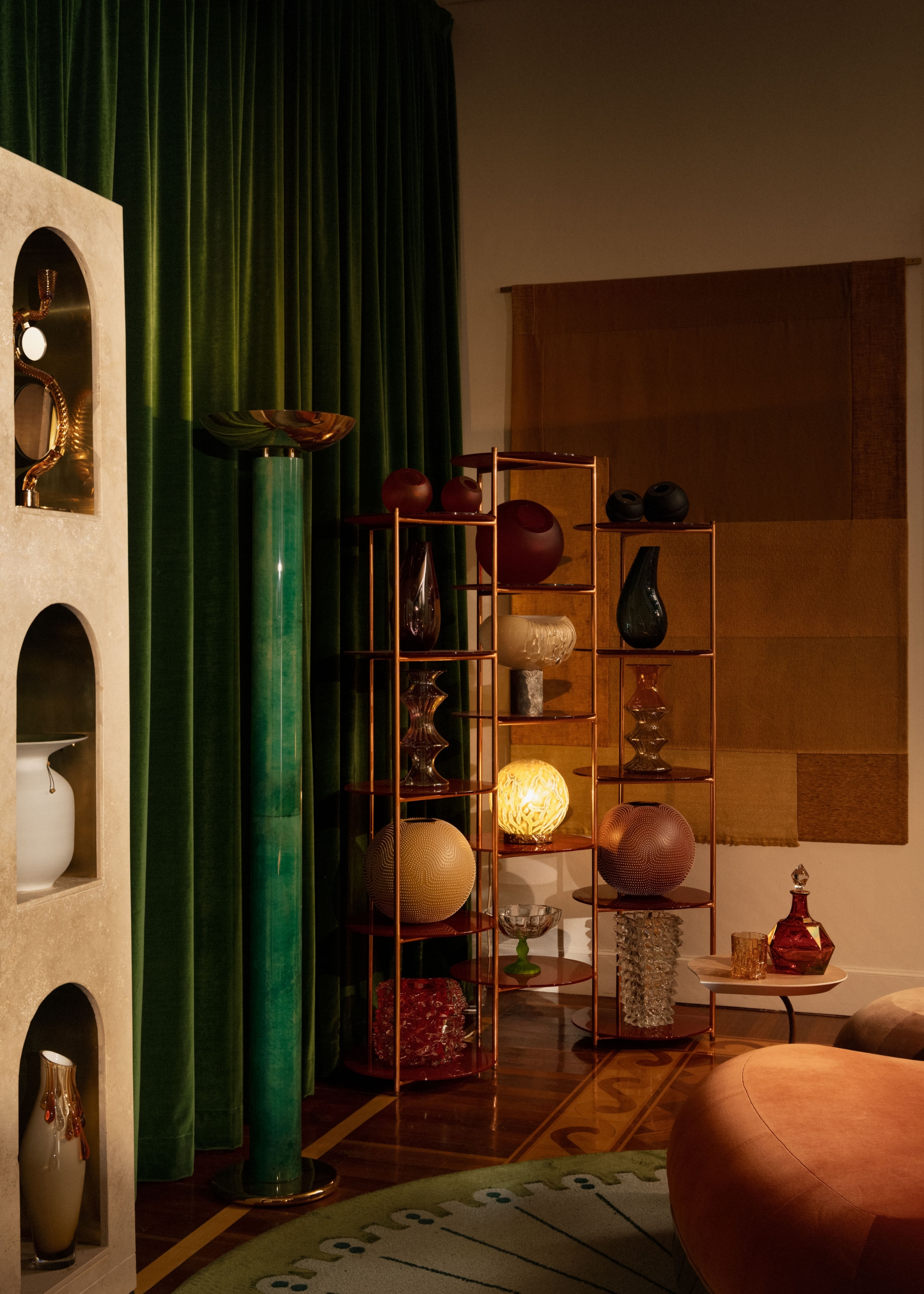 the corner of the entertainment room with circular decor on gold open shelving next to a cylindrical floor lamp and next to the circular rug and rounded seating