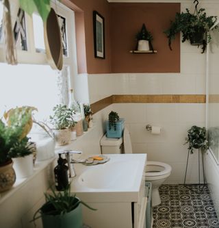 a small taupe boho bathroom with too many plants next to the sink and toilet