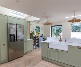 A sage green kitchen with hanging lights and large glazing