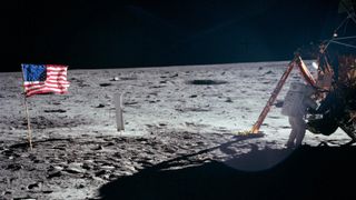 an astronaut in a spacesuit with a gold face shield walks on the grey dusty surface of the moon