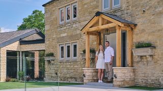 Young couple standing in the front porch of a stone cottage with contemporary extension