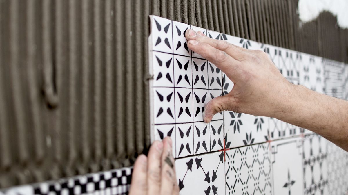 Hand pushing patterned tiles on tile adhesive on wall