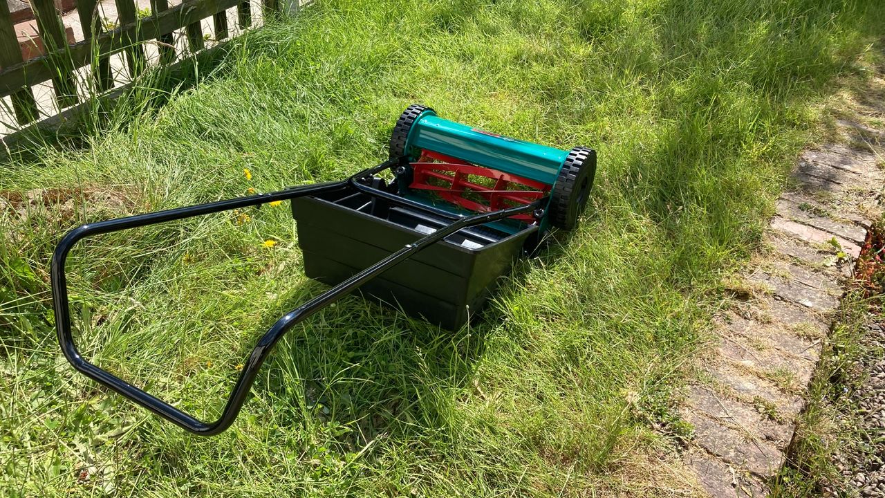 a Bosch AHM 38G manual push lawn mower on a patch of long grass in a cottage garden