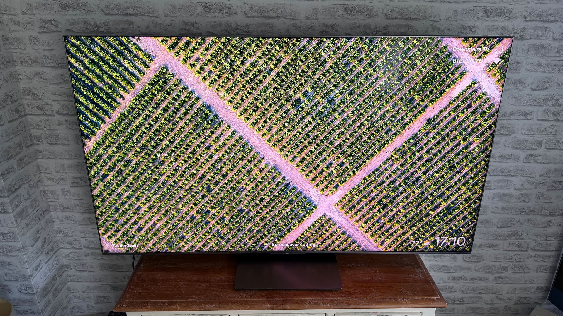 TCL C8L Mini LED TV in front of brick wall showing criss-crossing roads and trees