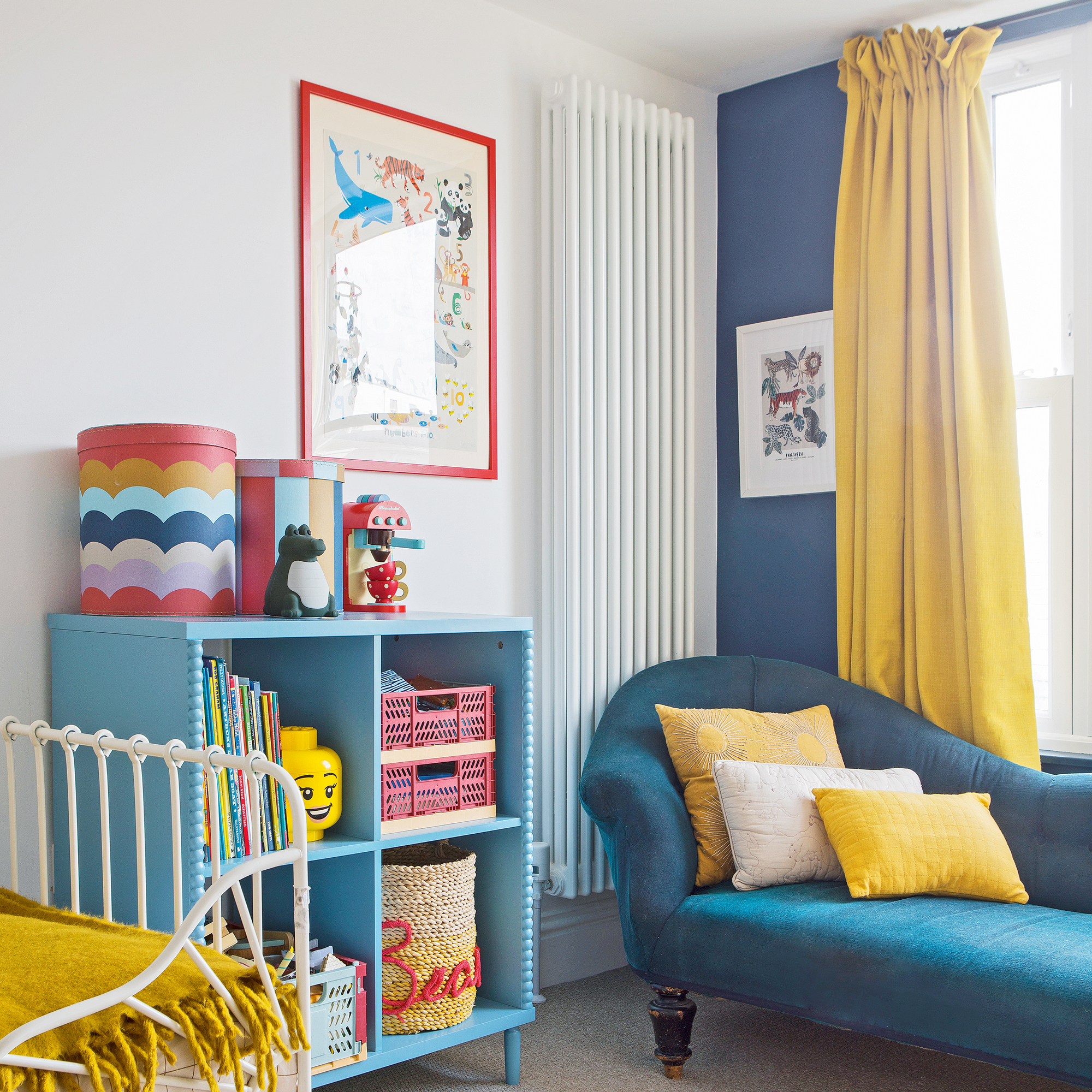 a kids room with a blue chaise and matching blue wall, yellow curtains and colourful storage units