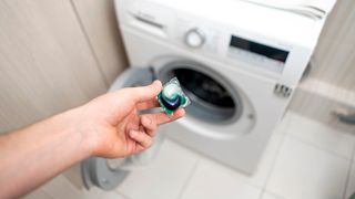 Someone holding a capsule of laundry detergent in front of a washing machine