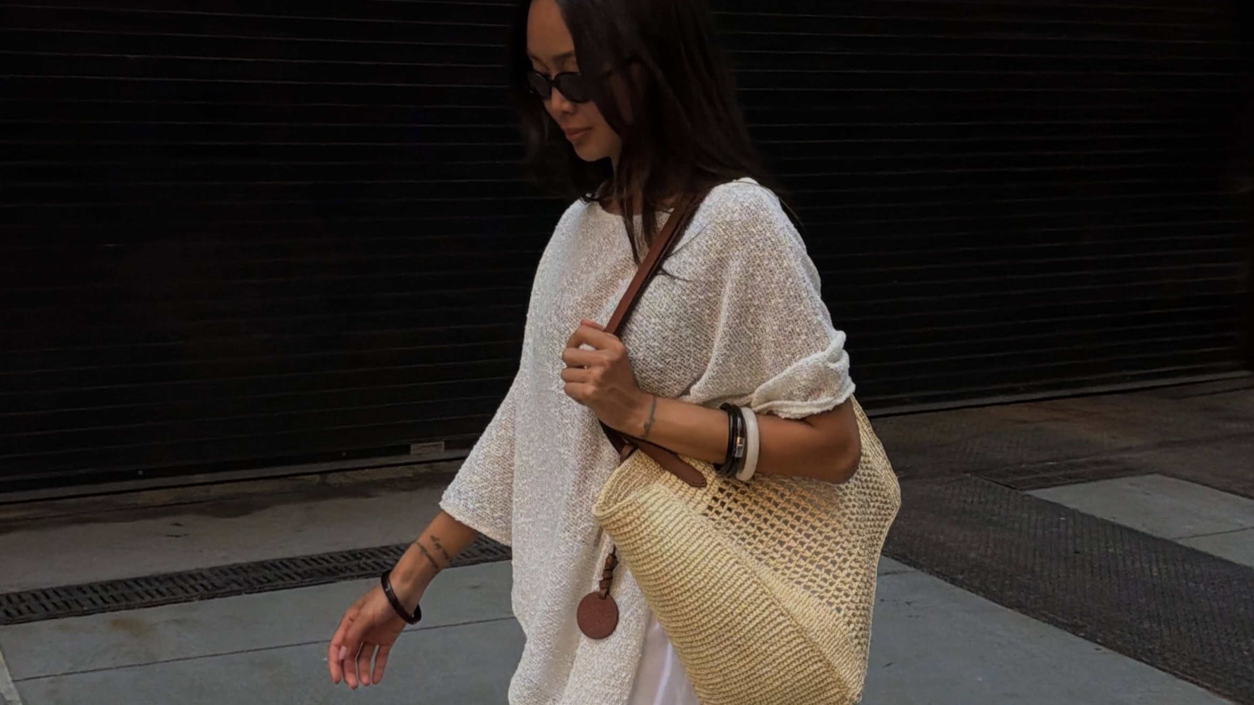 Woman wearing white shirt, raffia bag, and white shorts while wearing a ke summer 2026 shoe color trend, PVC shoes.