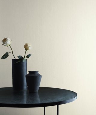 white wall with black round table with two black vases, one with rose stems