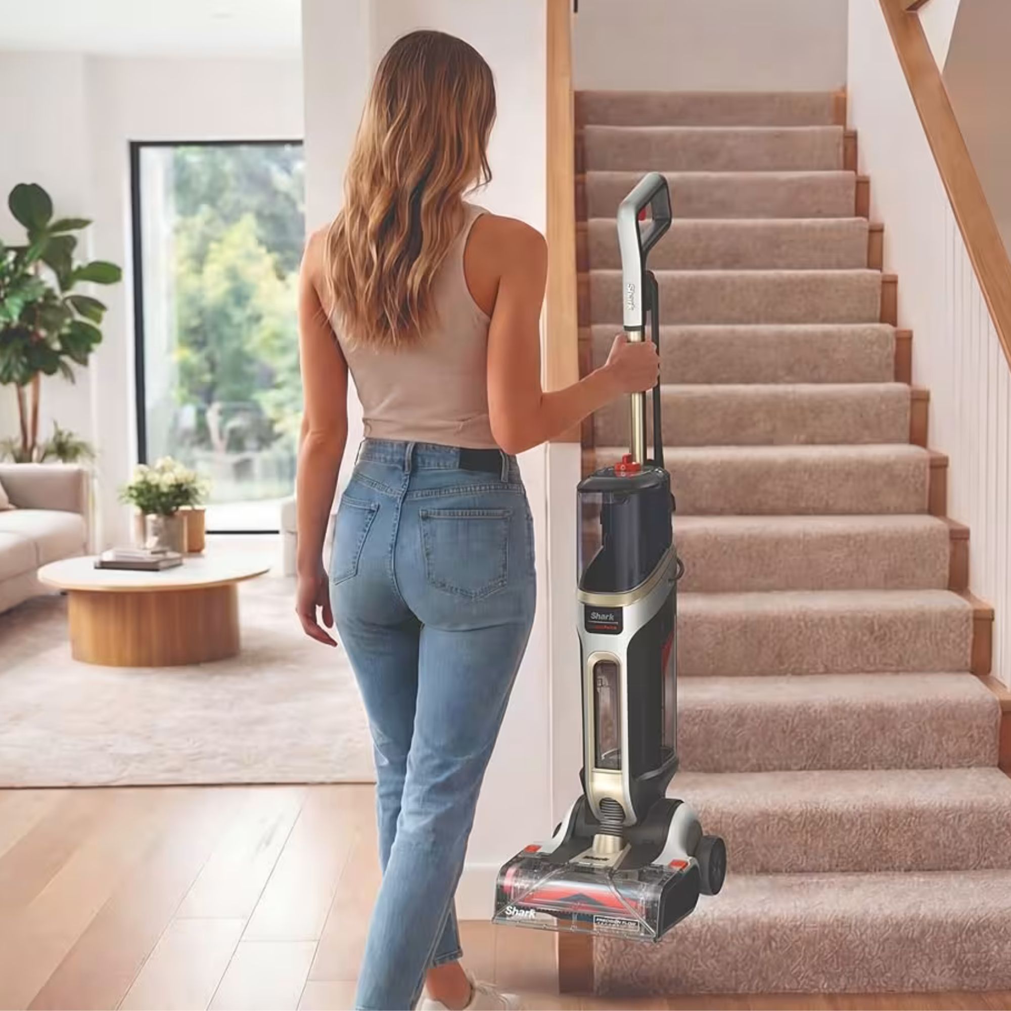 Woman carrying the Shark CarpetForce Upright Carpet Cleaner up cream carpeted stairs in a modern house