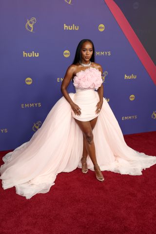 Aja Naomi King wears a pink minidress with a long train and pink flowers as well as silver heels and a large diamond choker necklace.